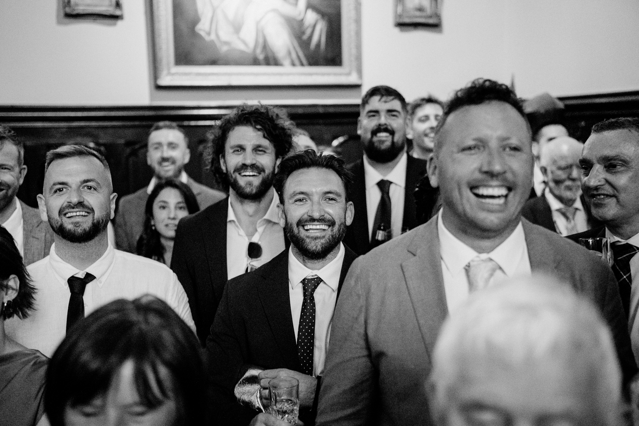 Black and white candid photograph of male wedding guests laughing during speeches at Markree Castle.