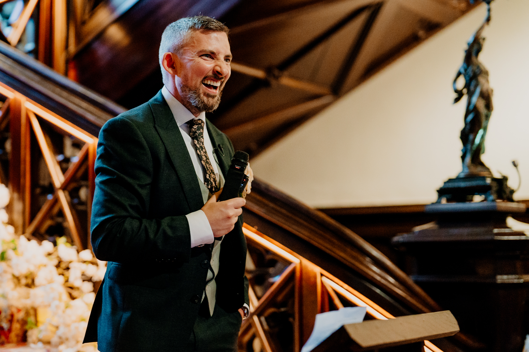 Groom Mark smiling while delivering a wedding speech with a microphone on the grand staircase at Markree Castle.