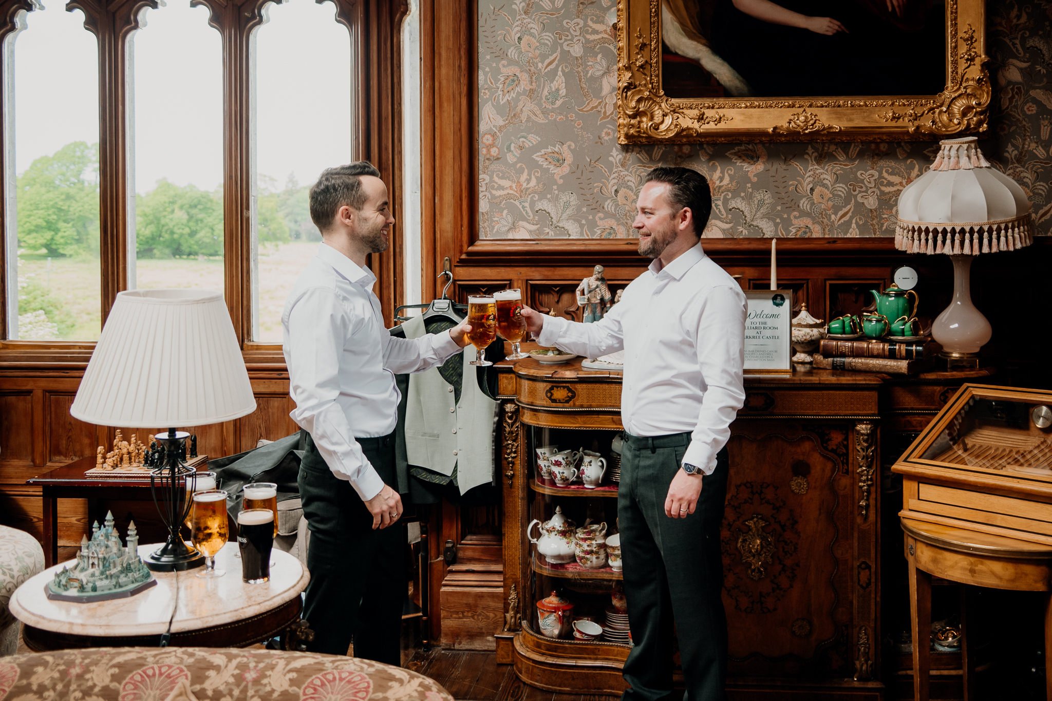 Groom and groomsman raising a toast during wedding morning preparations in the Billiard Room at Markree Castle.