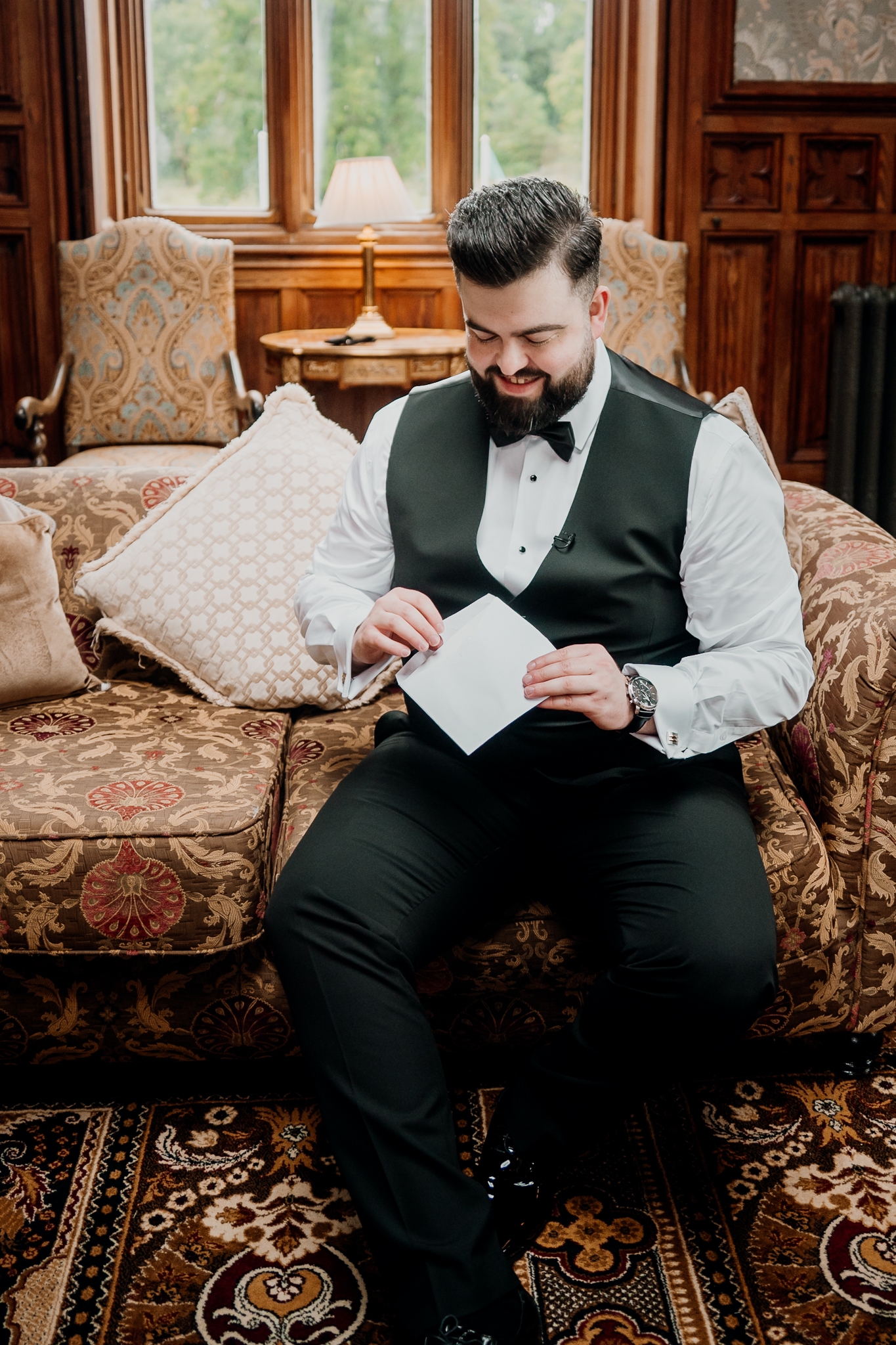 Groom in a black waistcoat and bow tie looking down while fastening his outfit during wedding preparations at Markree Castle.