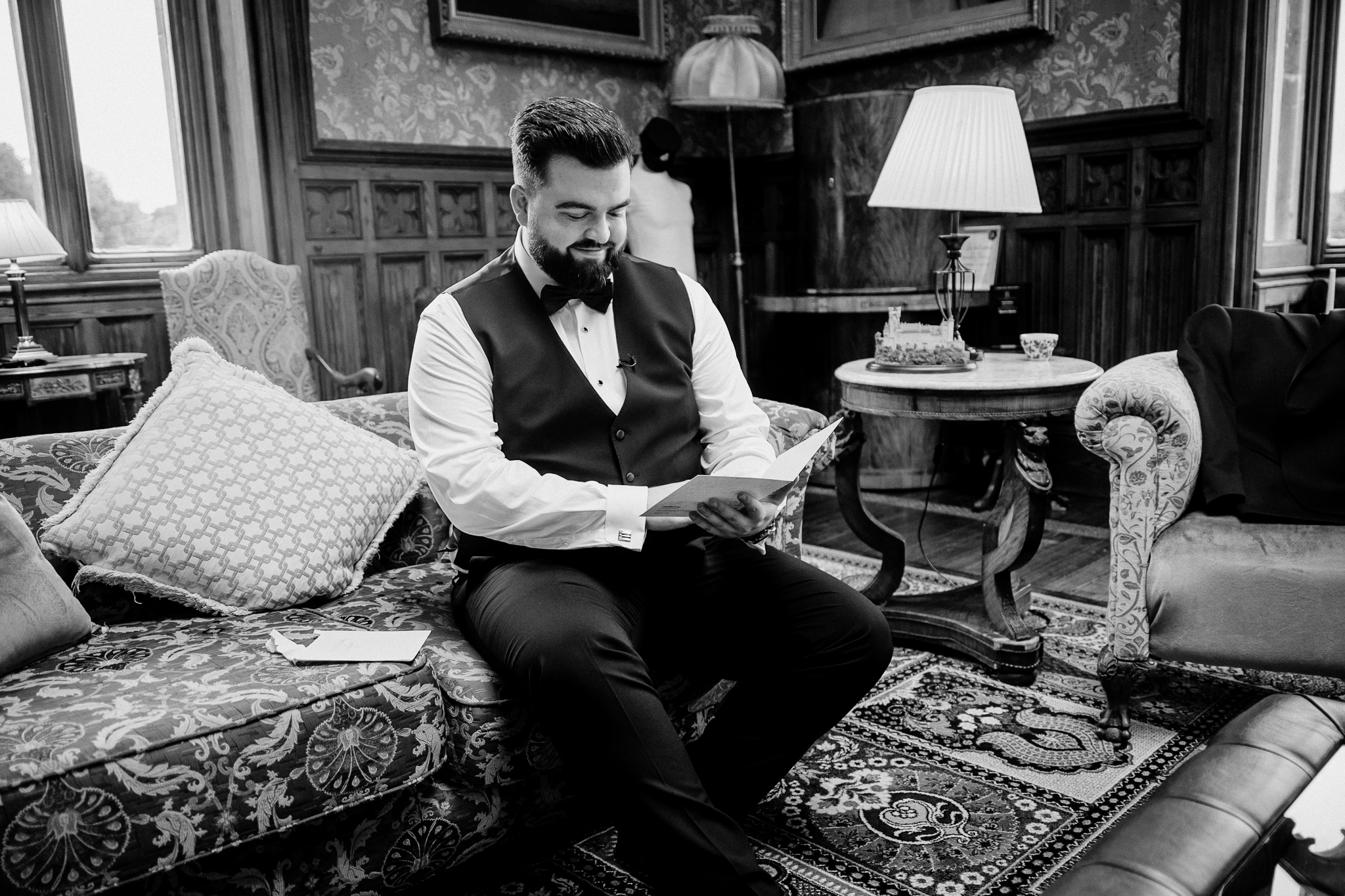 Black and white photograph of groom Anthony reading a letter while seated in the Billiard Room at Markree Castle.