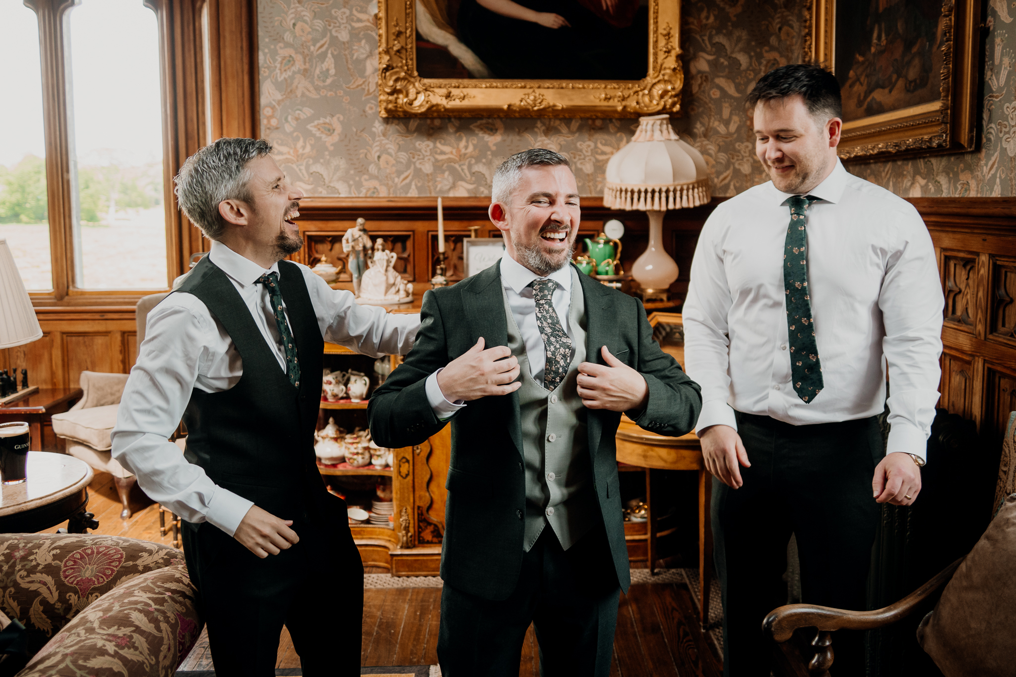 Groom and groomsmen laughing together with drinks during wedding preparations in the Billiard Room at Markree Castle.