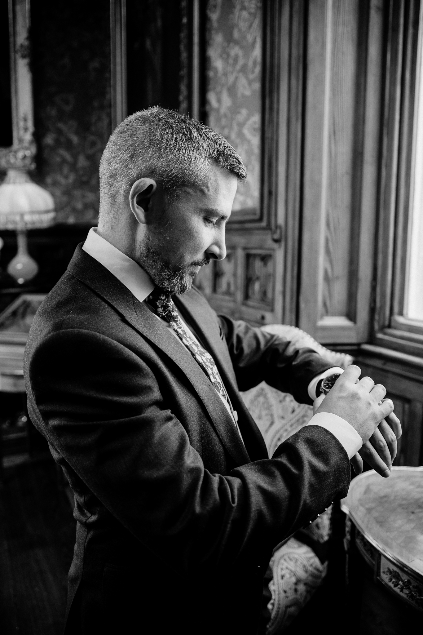 Black and white portrait of a groom adjusting his wristwatch beside a window at Markree Castle.