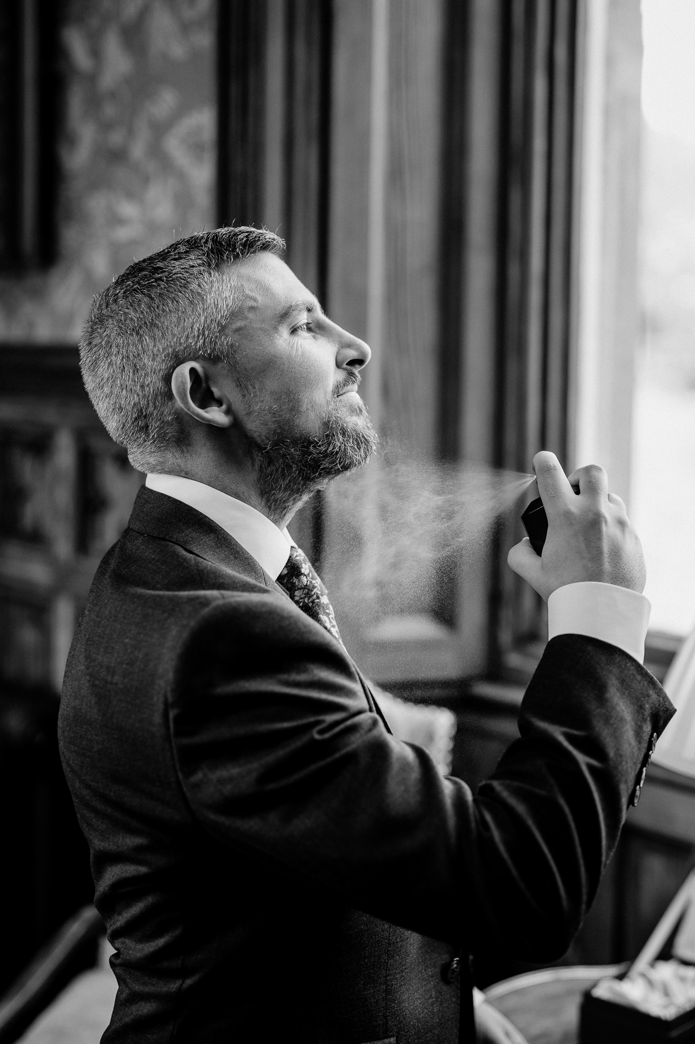 Groom applying cologne beside a window during wedding morning preparations at Markree Castle.