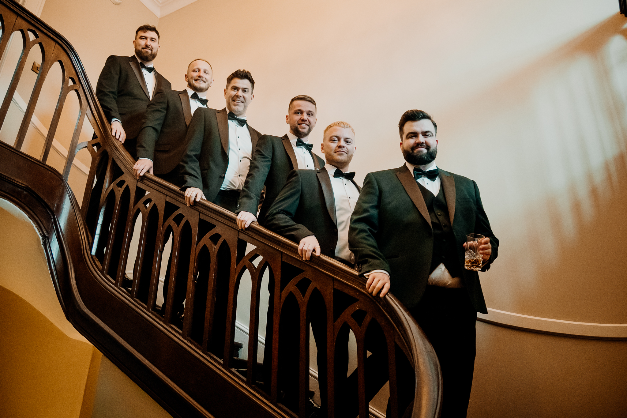Groom and groomsmen in dark green suits posing together on the grand staircase at Markree Castle.
