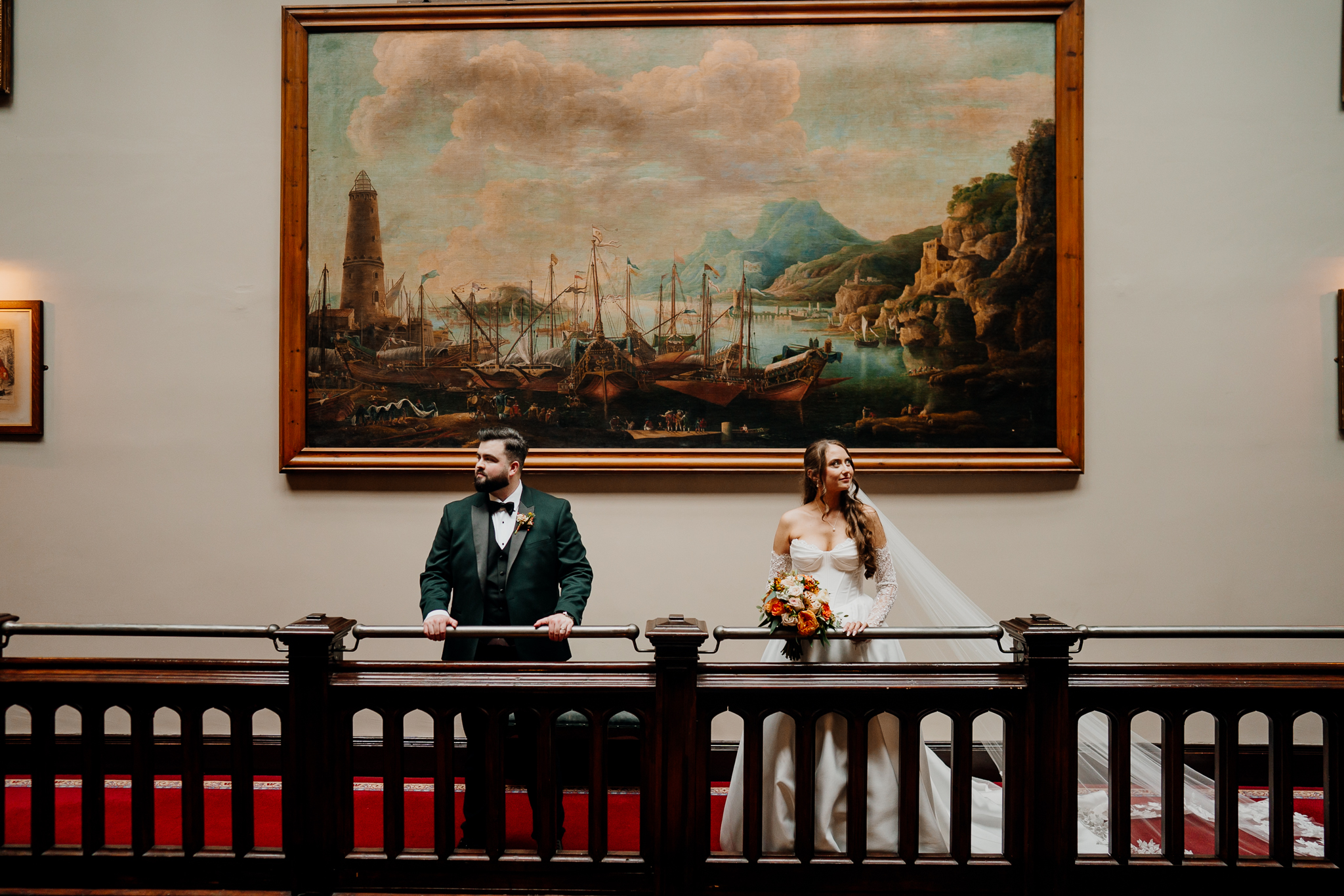 Bride and groom kissing beneath a large historic painting on the gallery balcony at Markree Castle.