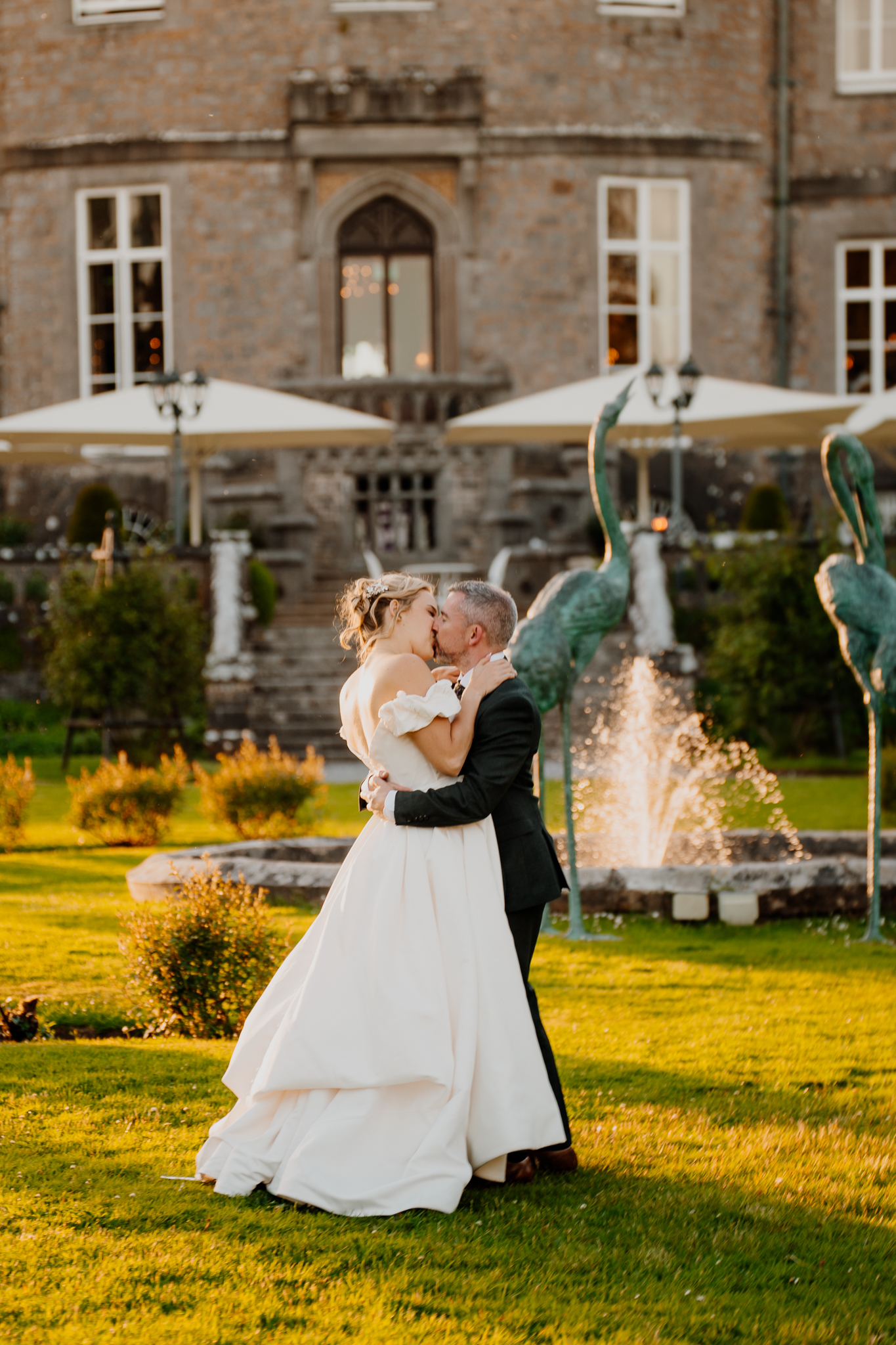 Bride and groom embracing beside decorative peacock sculptures in the gardens of Markree Castle during golden hour.