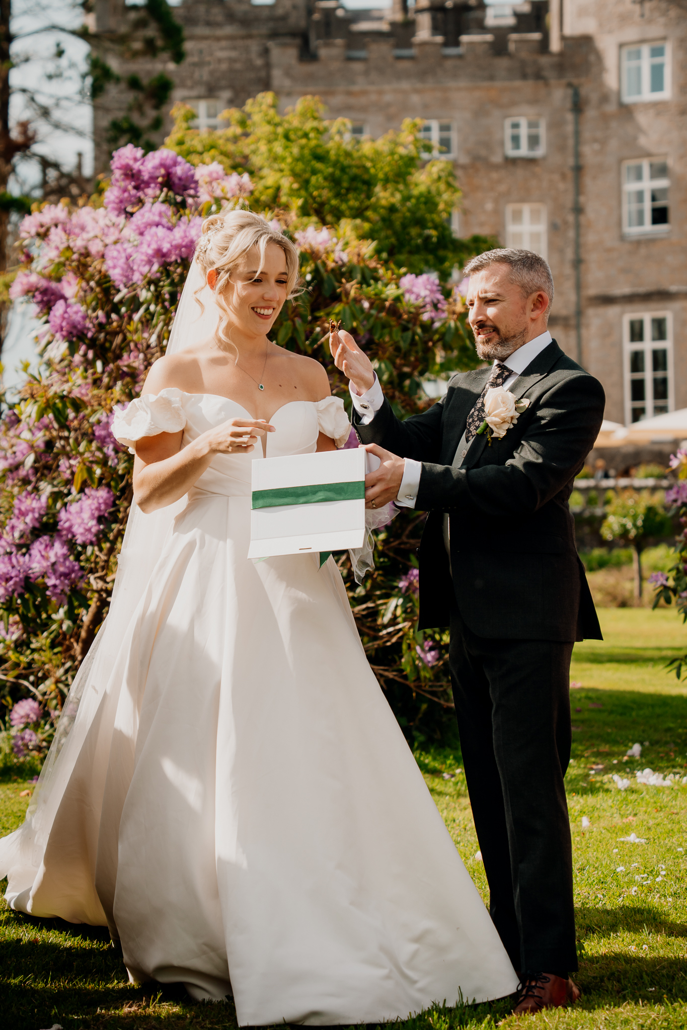 Bride Zoe and groom Mark smiling as they open a butterfly release box during their Markree Castle garden wedding reception.