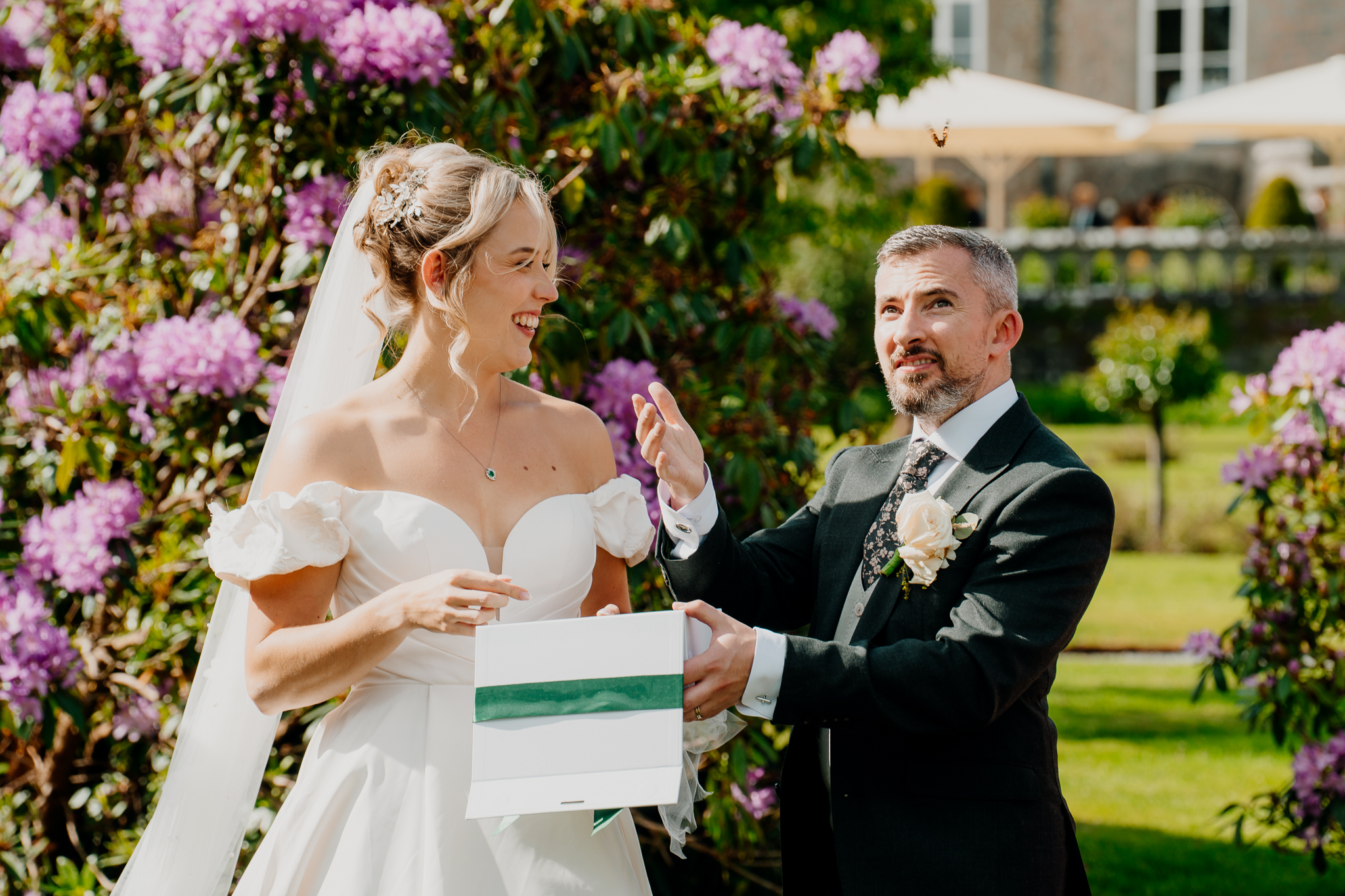 Bride and groom smiling during their wedding butterfly release beside pink flowering shrubs at Markree Castle.