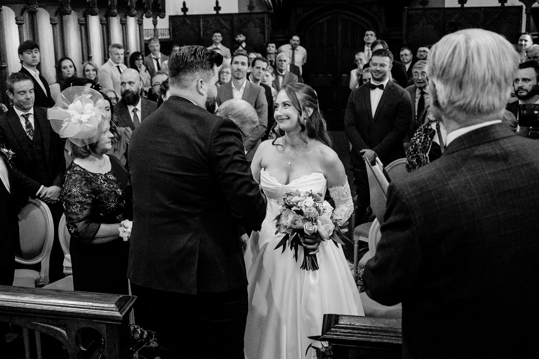 Black and white candid photograph of wedding guests and the bride during the ceremony inside Markree Castle Chapel.