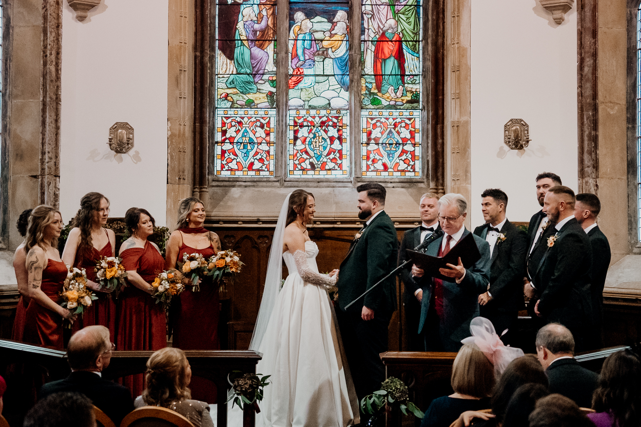 Wedding ceremony inside Markree Castle Chapel with colourful stained glass windows behind the altar.