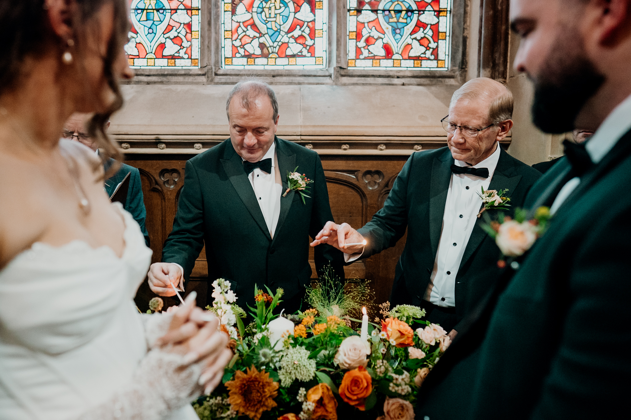 Two men seated at a table during the wedding ceremony inside Markree Castle Chapel, with stained glass windows behind them.