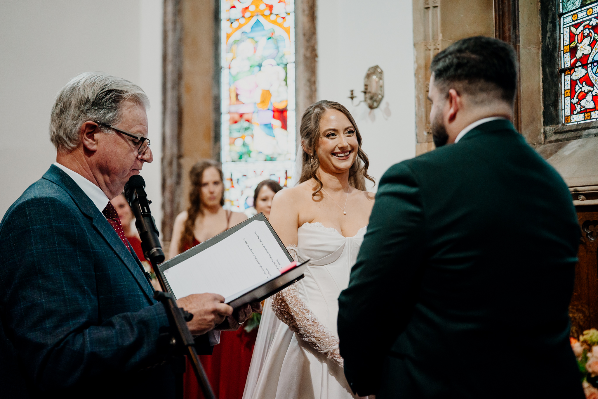 Bride smiling at the groom during their wedding vows inside Markree Castle Chapel, with stained glass windows in the background.