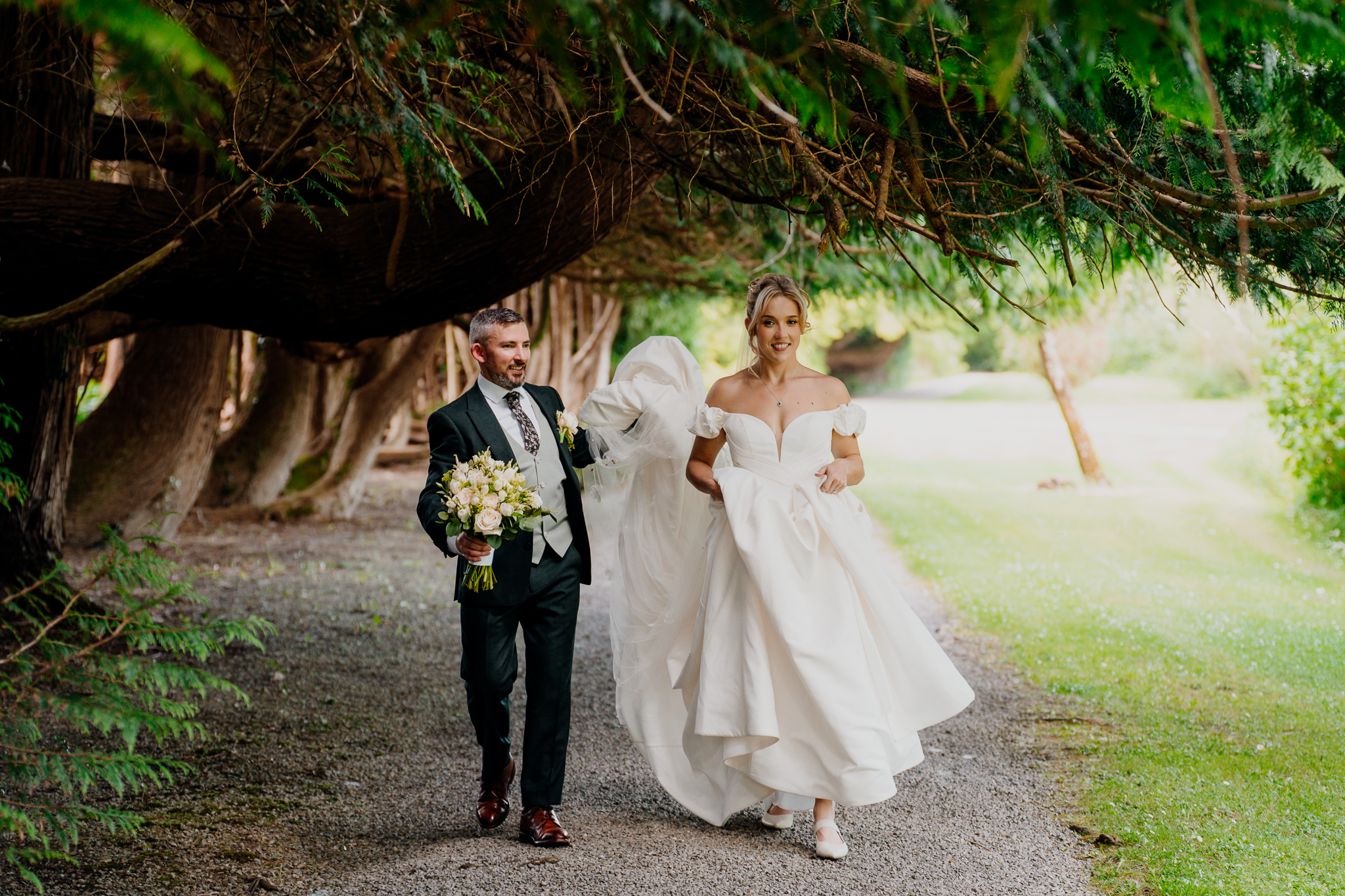 Bride Zoe and groom Mark walking together beneath sweeping tree branches during their Markree Castle wedding portraits.