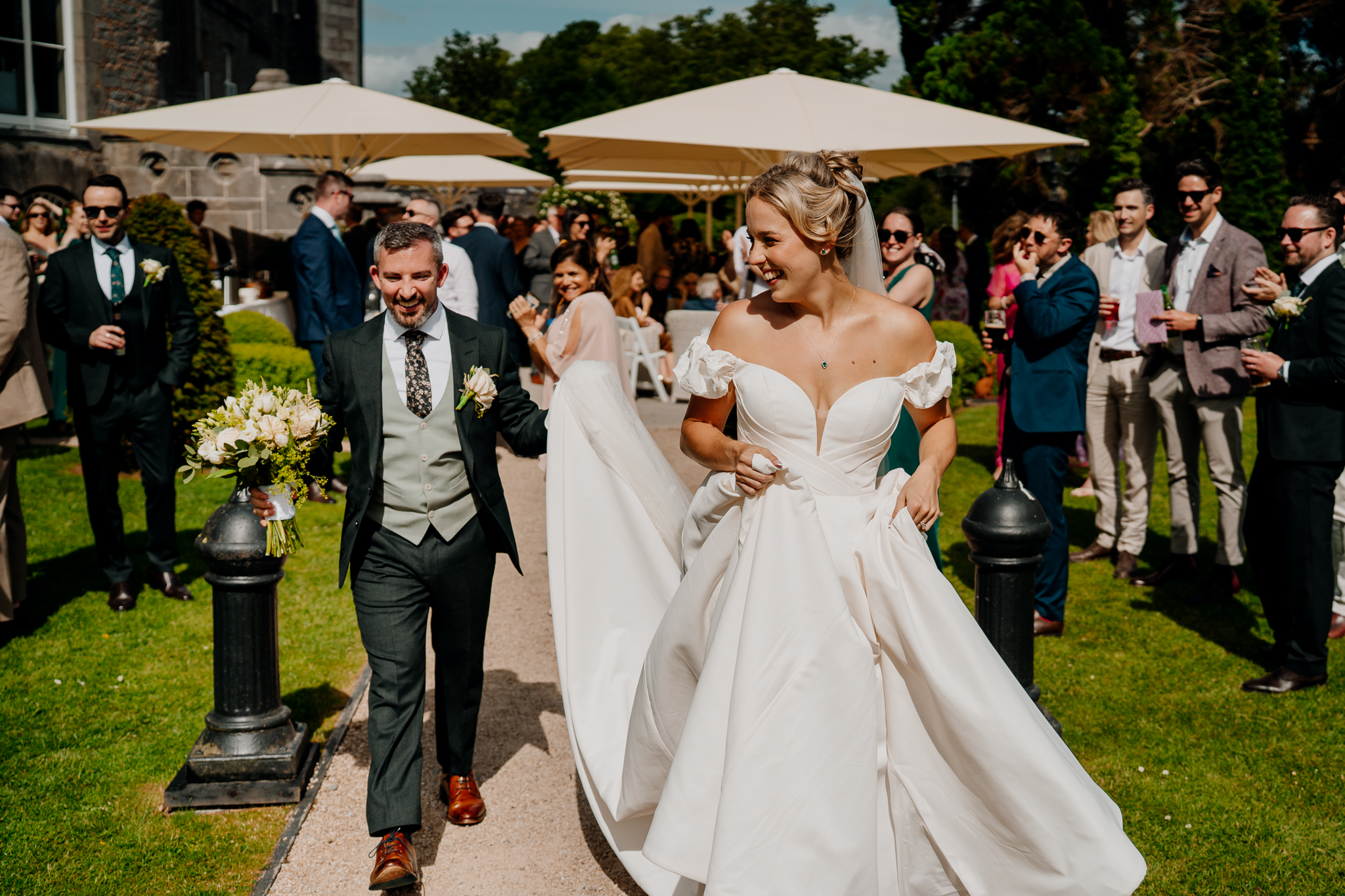 Bride and groom walking together past wedding guests and outdoor parasols in the gardens of Markree Castle.