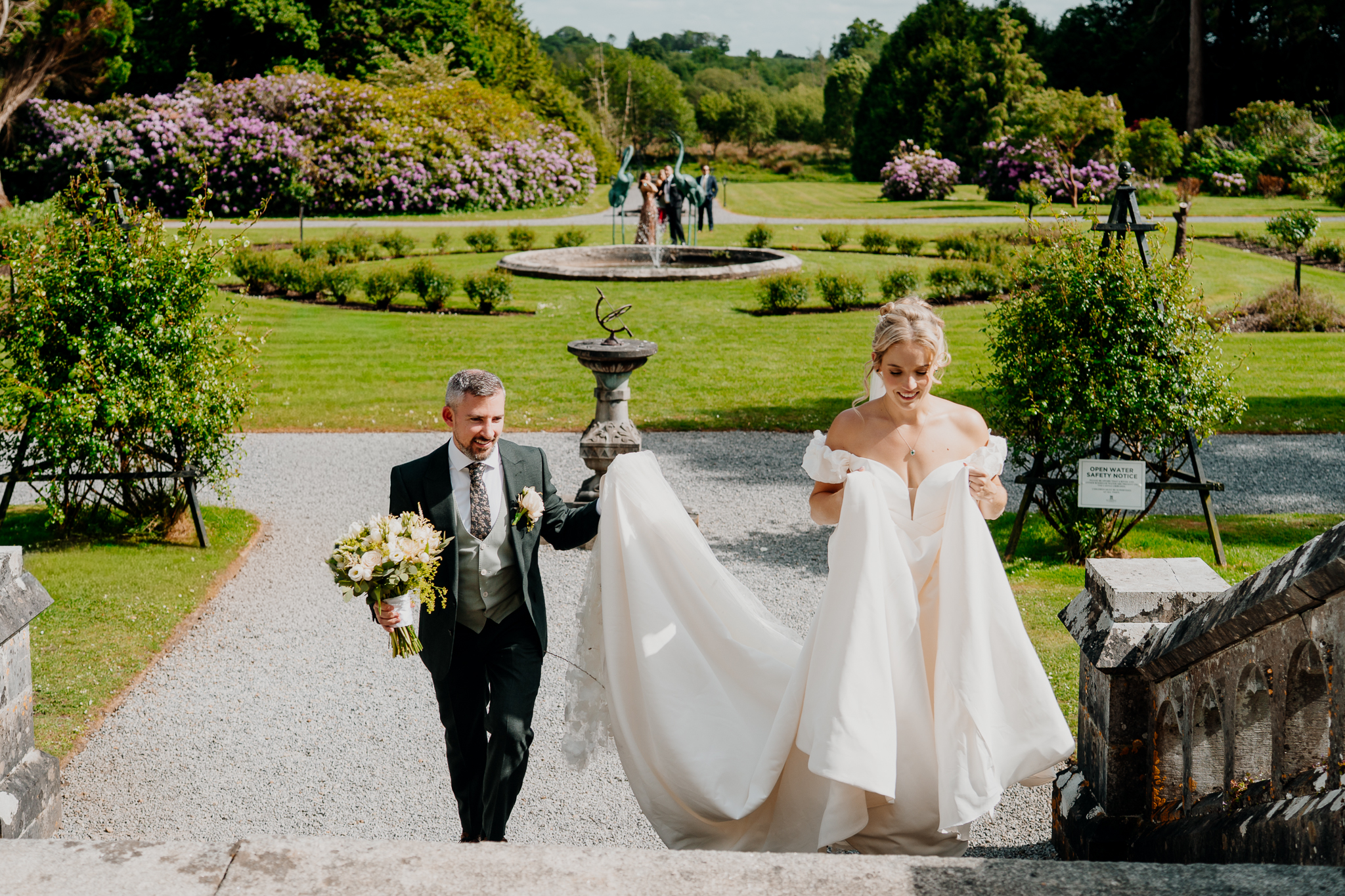 Bride and groom walking beside a garden fountain and flower beds at Markree Castle in County Sligo.