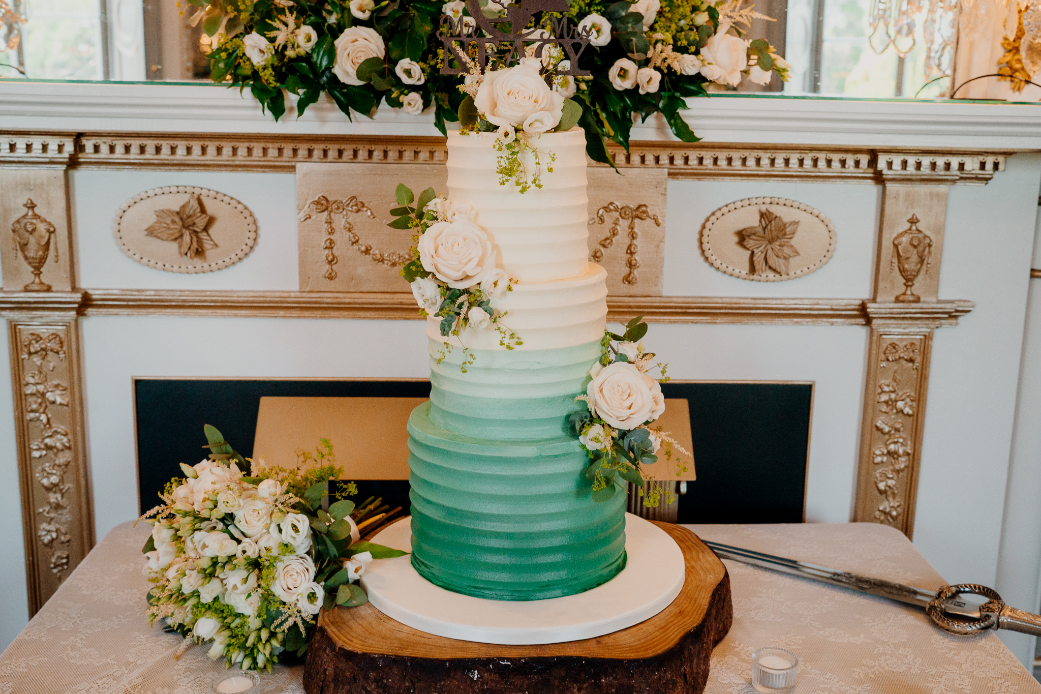 Elegant tiered wedding cake decorated with white roses and greenery inside Markree Castle in County Sligo.