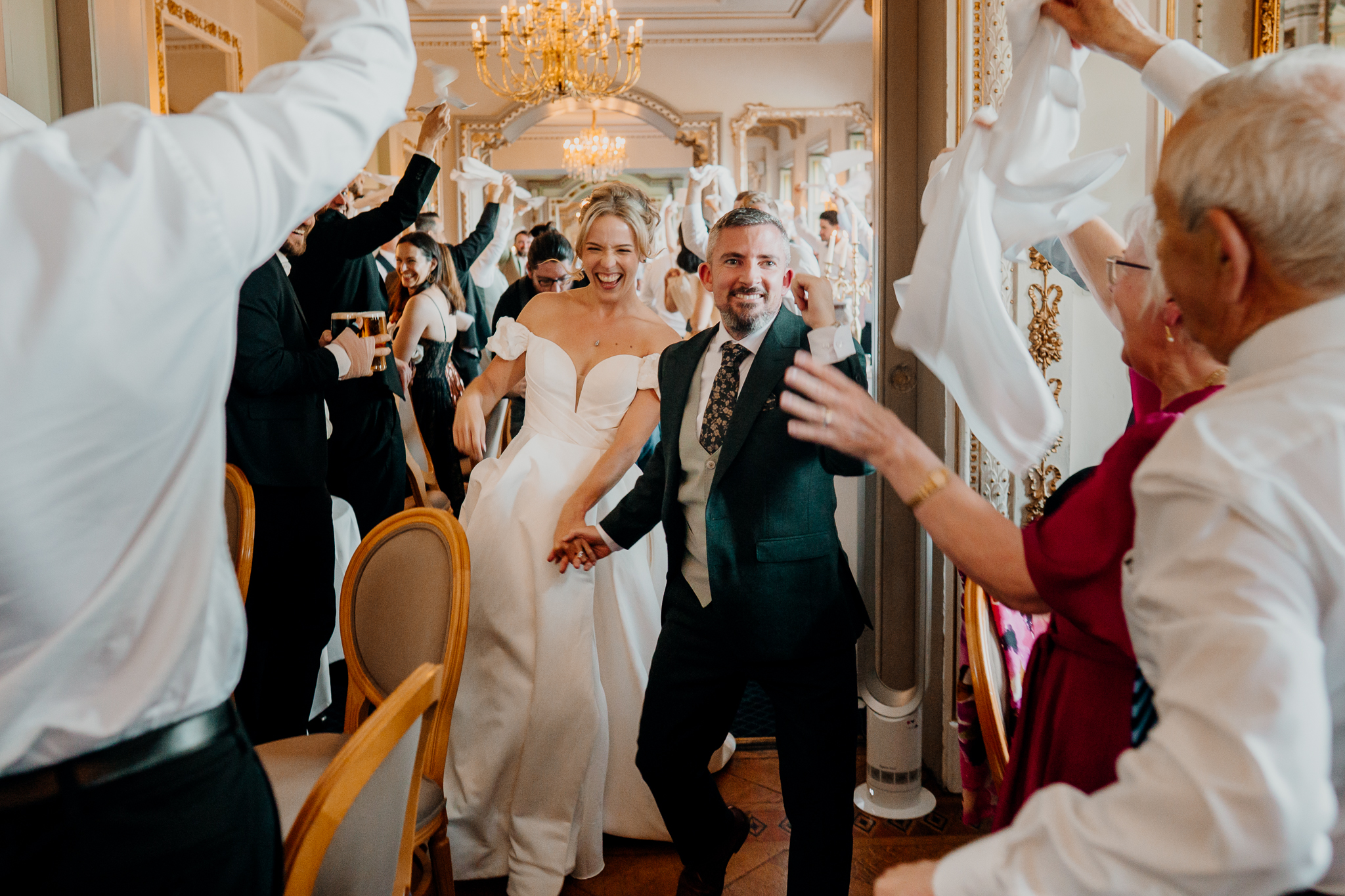 Bride Zoe and groom Mark entering the grand Dining Room at Markree Castle as wedding guests cheer and wave napkins.