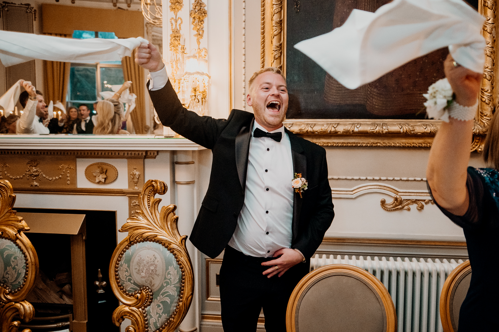 Male wedding guest cheering with his arm raised during the evening celebrations in Markree Castle's dining room.
