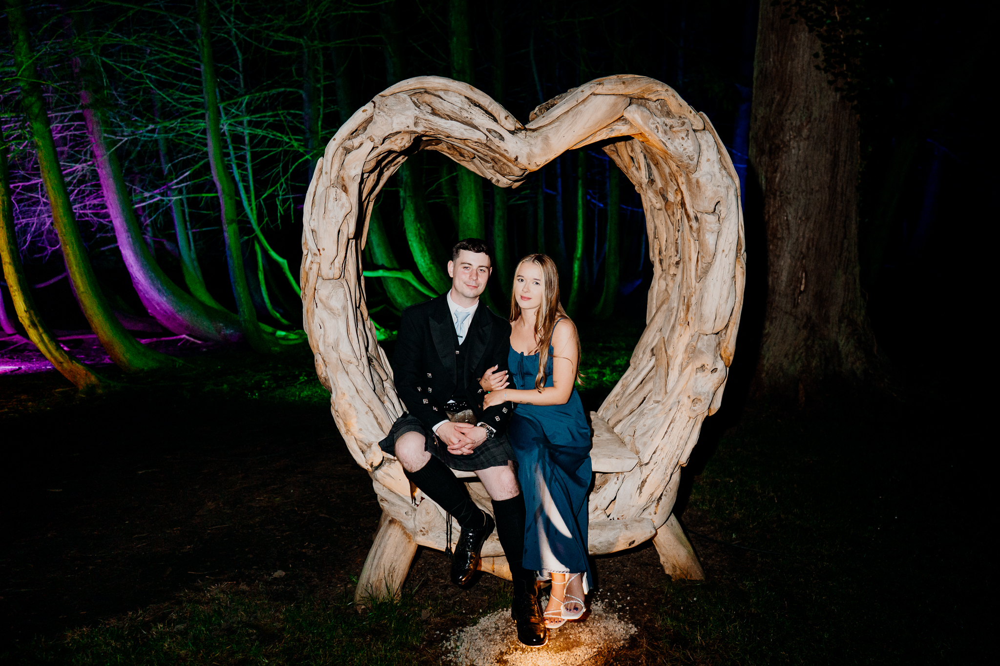 Wedding guests posing inside an illuminated heart installation at Markree Castle Woodlands at night.