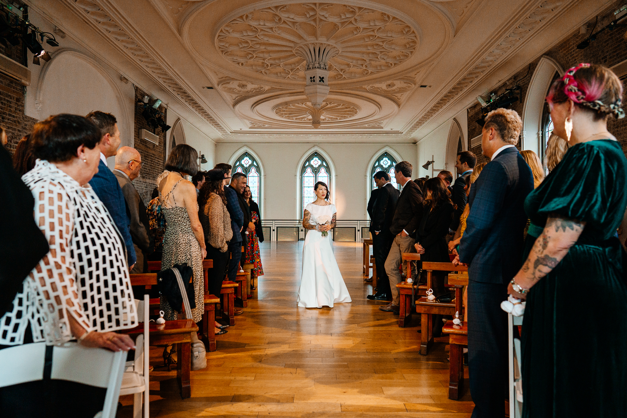 Bride walking down the aisle between wedding guests during her ceremony at Smock Alley Theatre in Dublin, Ireland